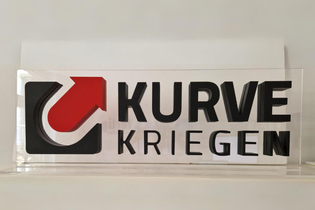 Logo "KURVE KRIEGEN" als T-Aufsteller